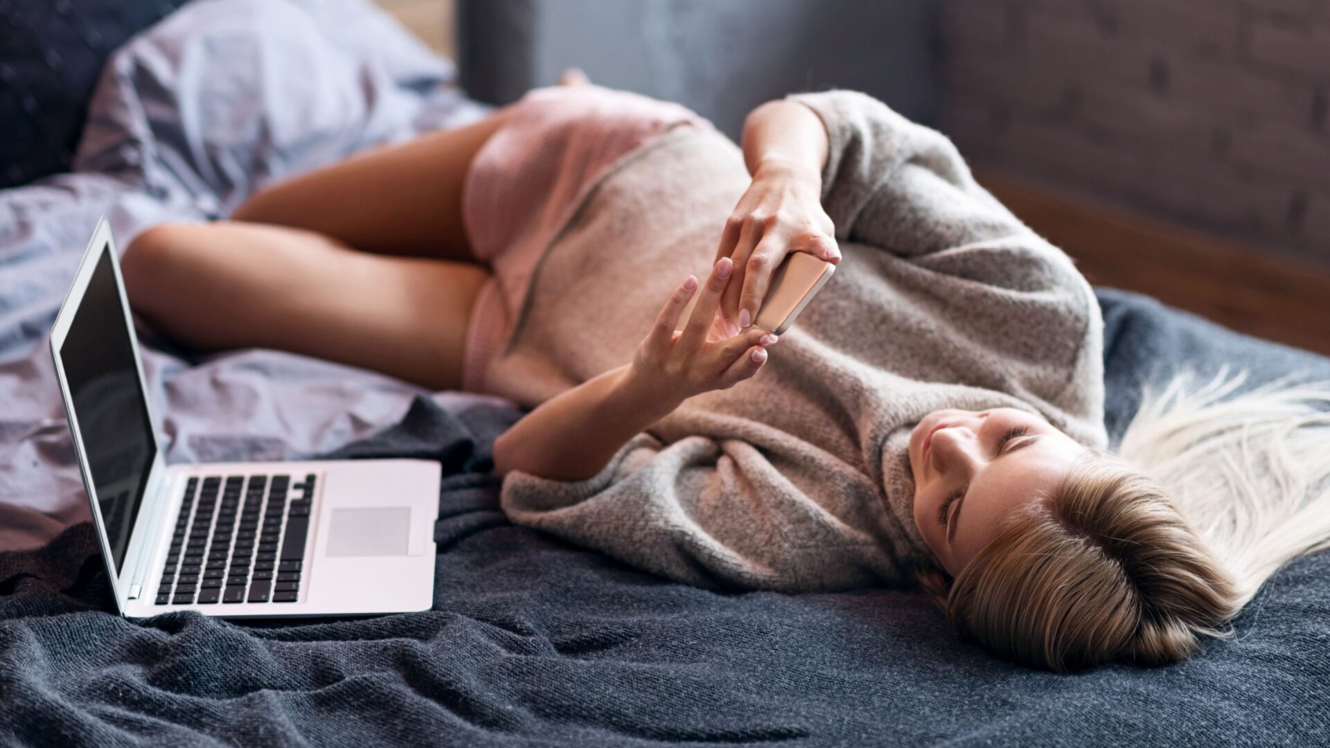 vrouw op bed met laptop en telefoon