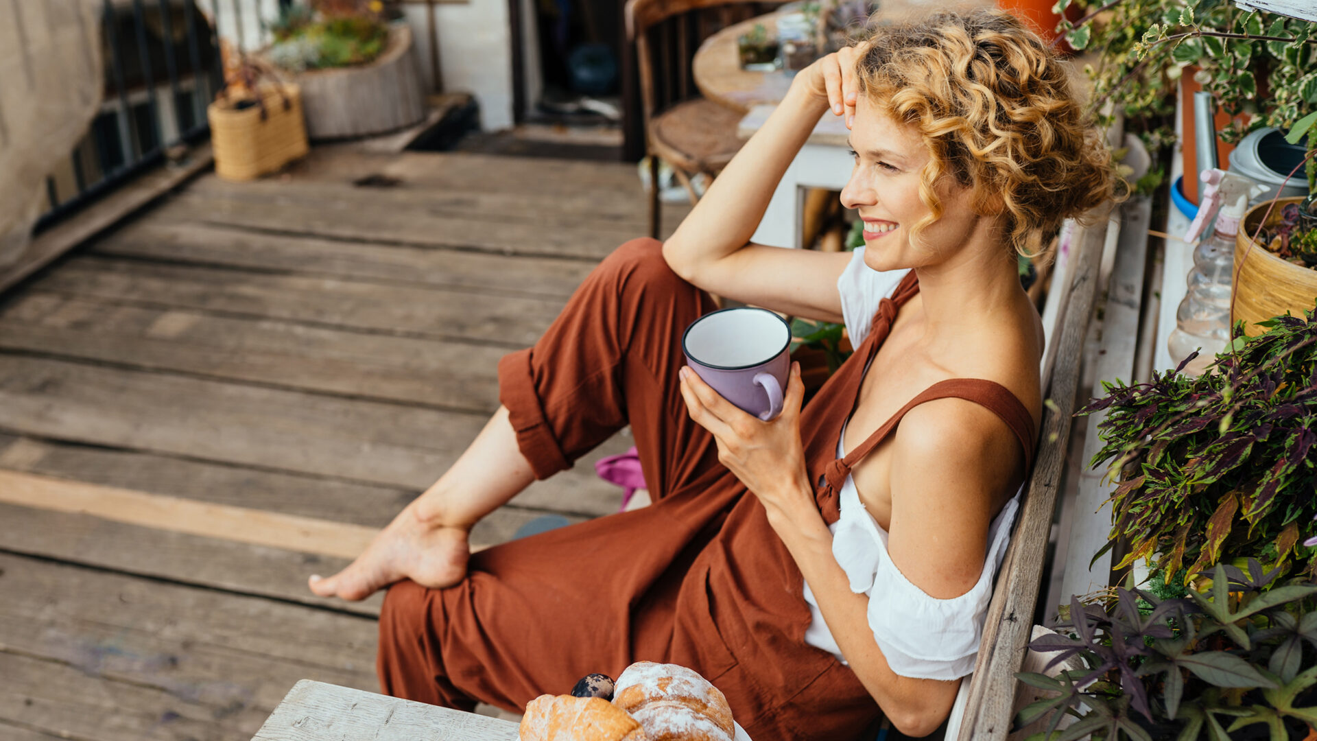 vrouw met roestbruine tuinbroek aan drinkt een kop koffie op haar patio