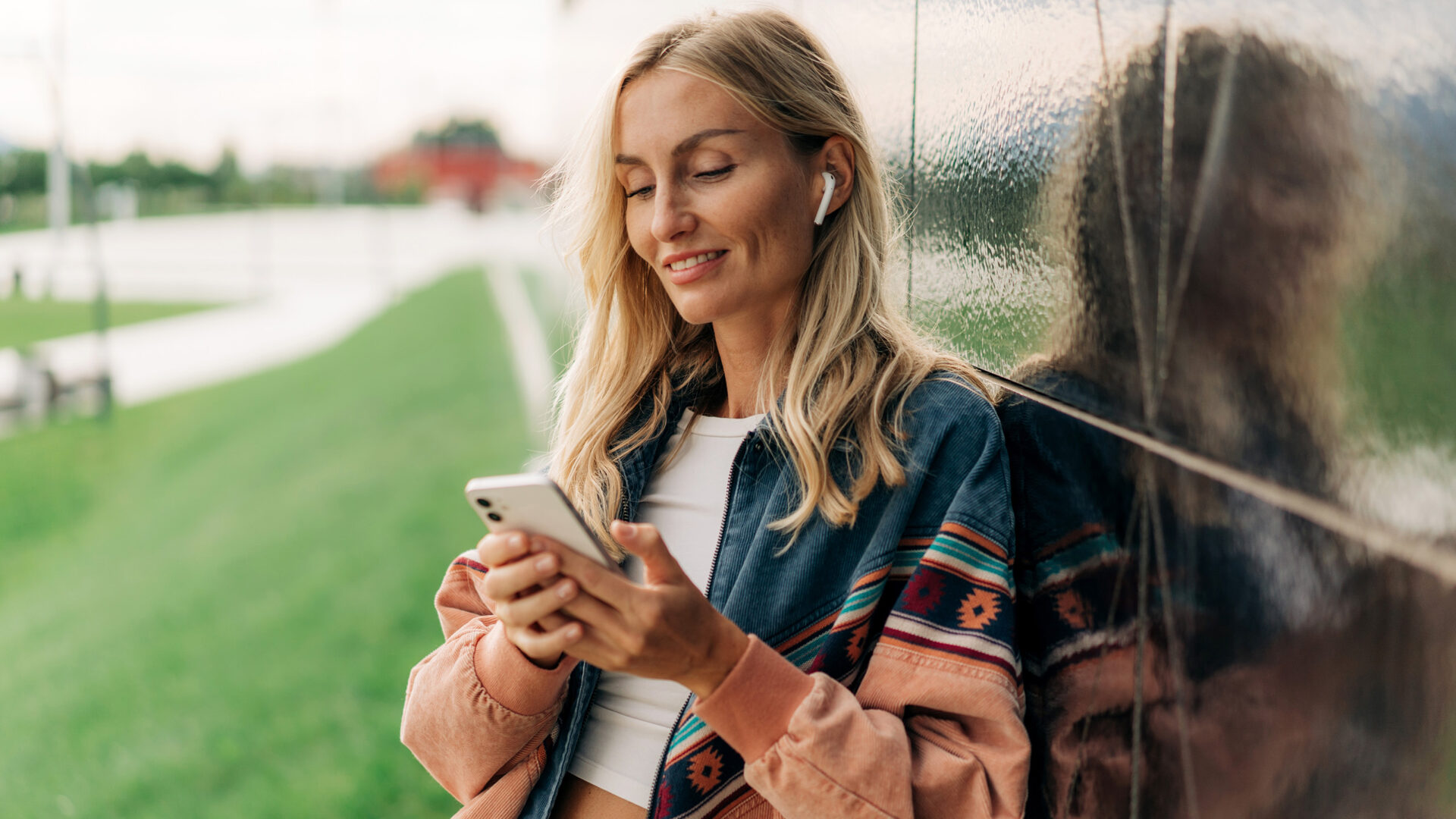 Vrouw leunt tegen muur aan en kijkt op mobiele telefoon