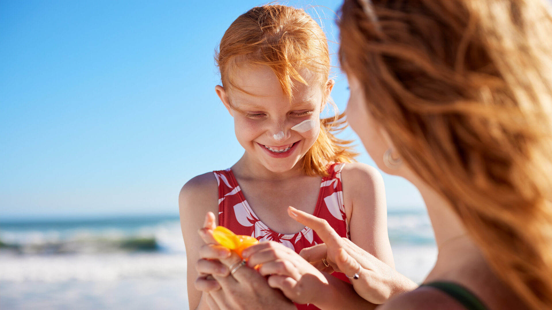 Vrouw en kind met zonneproduct op het strand