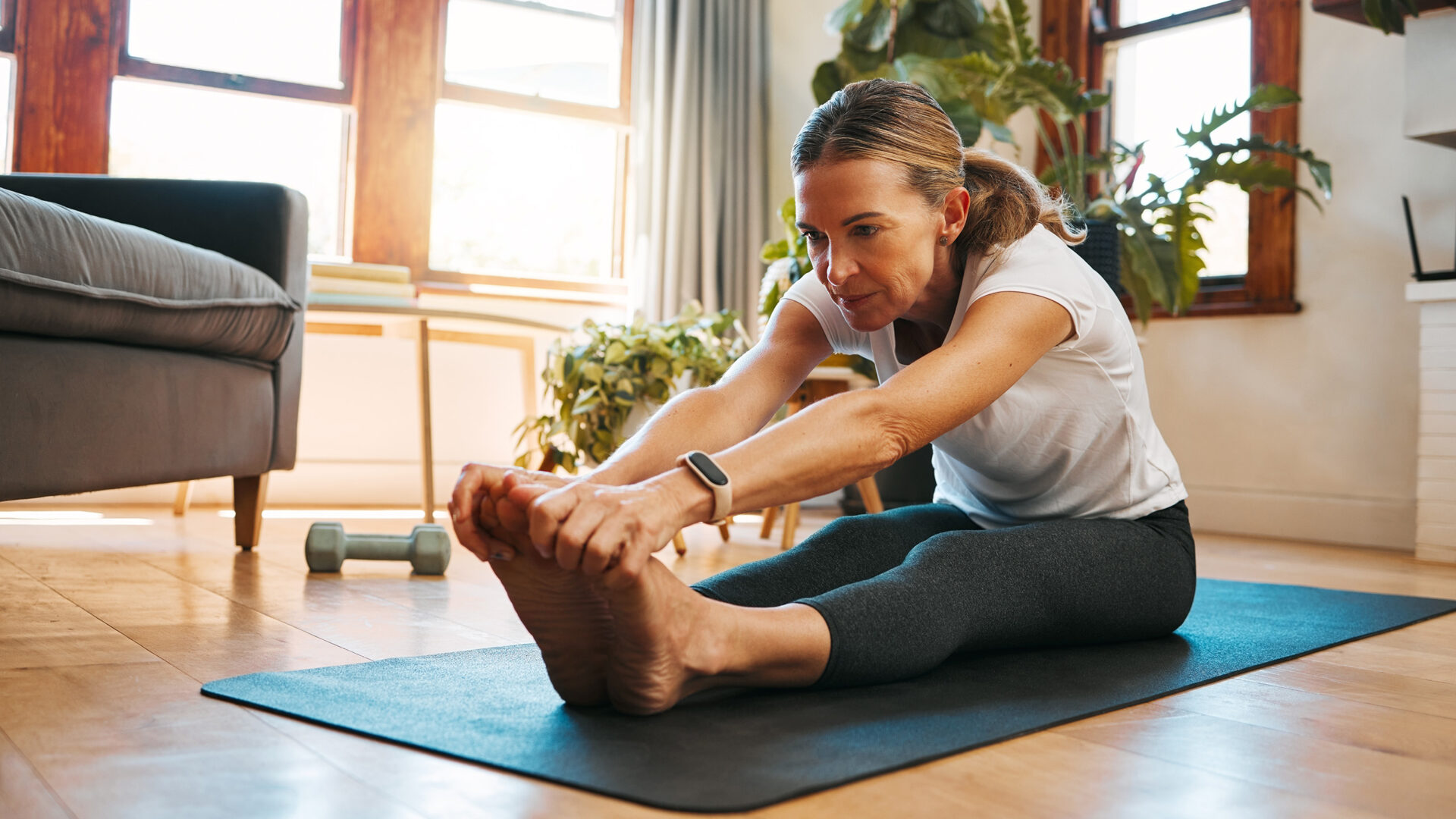 vrouw op yogamat strekt zittend met haar handen naar haar tenen