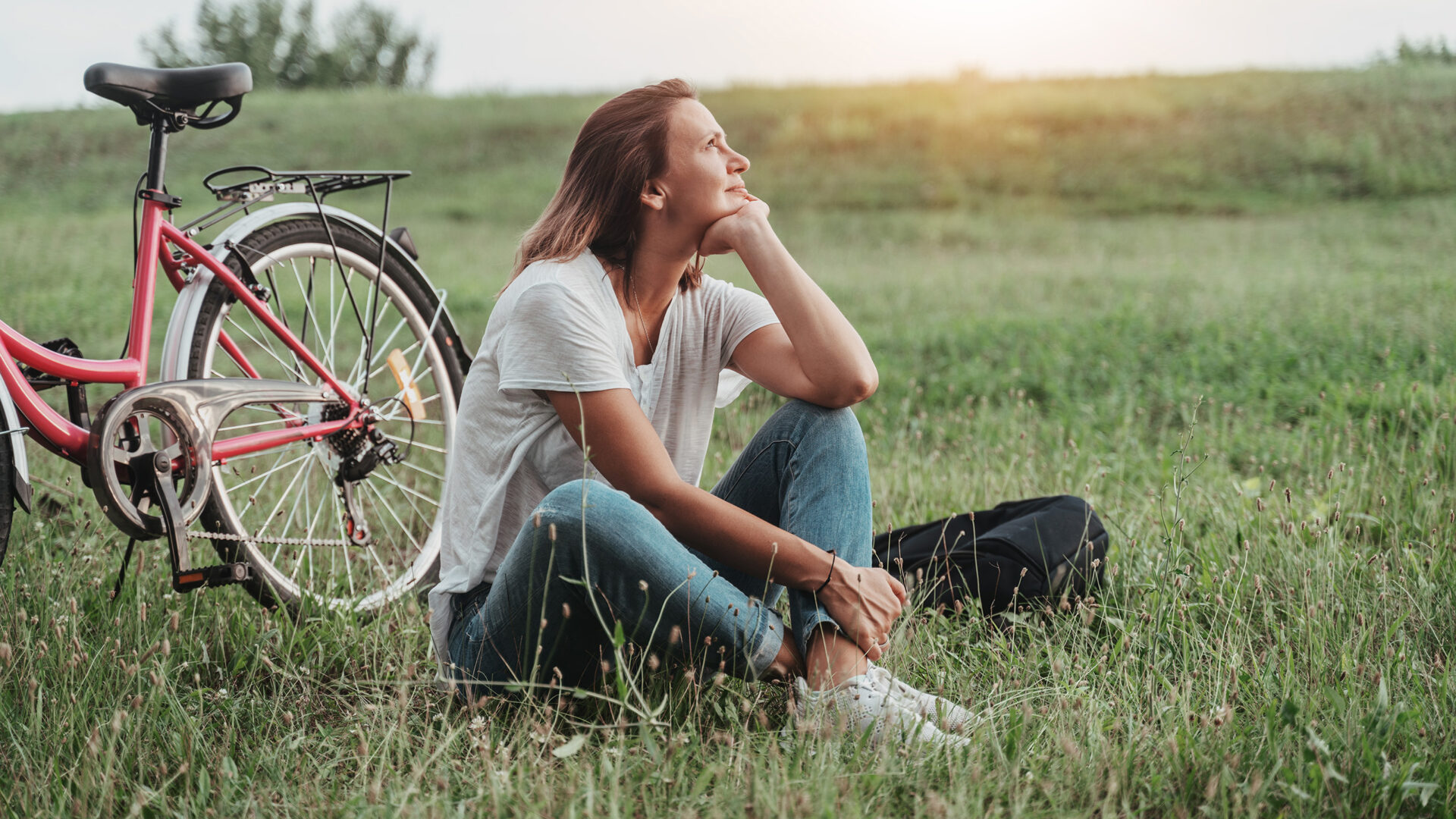 Vrouw in de kleermakerszit op het gras, naast haar staat een fiets