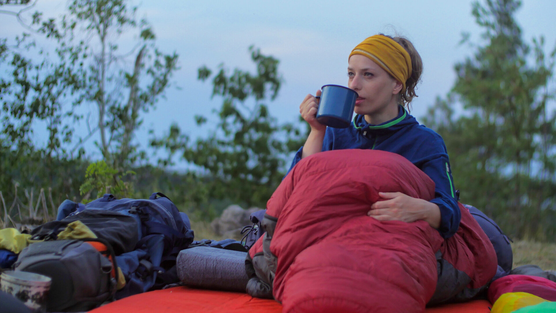 Vrouw in een slaapzak in de buitenlucht met een mok in haar handen