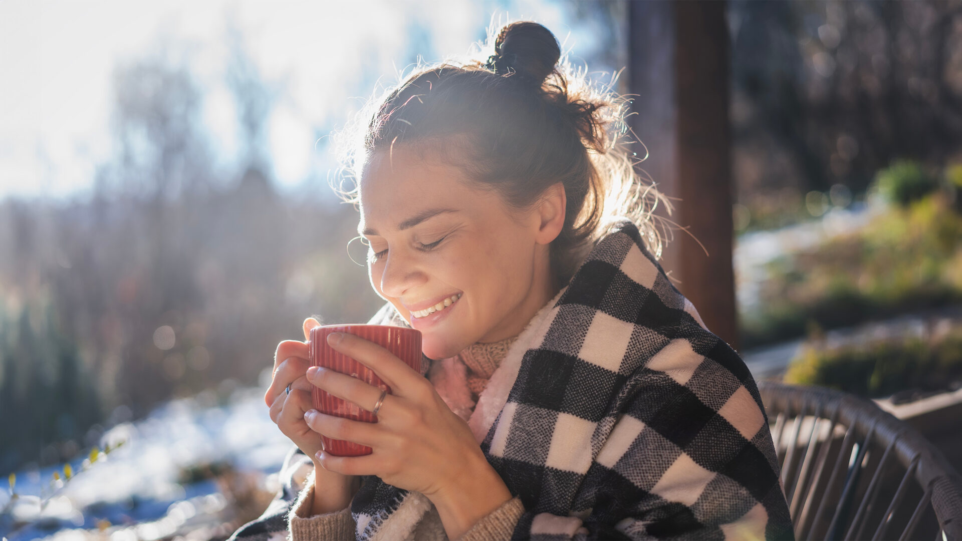 Vrouw buiten met een mok in haar handen en een plaid om haar schouders