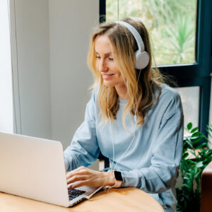 Vrouw met koptelefoon achter laptop in huis