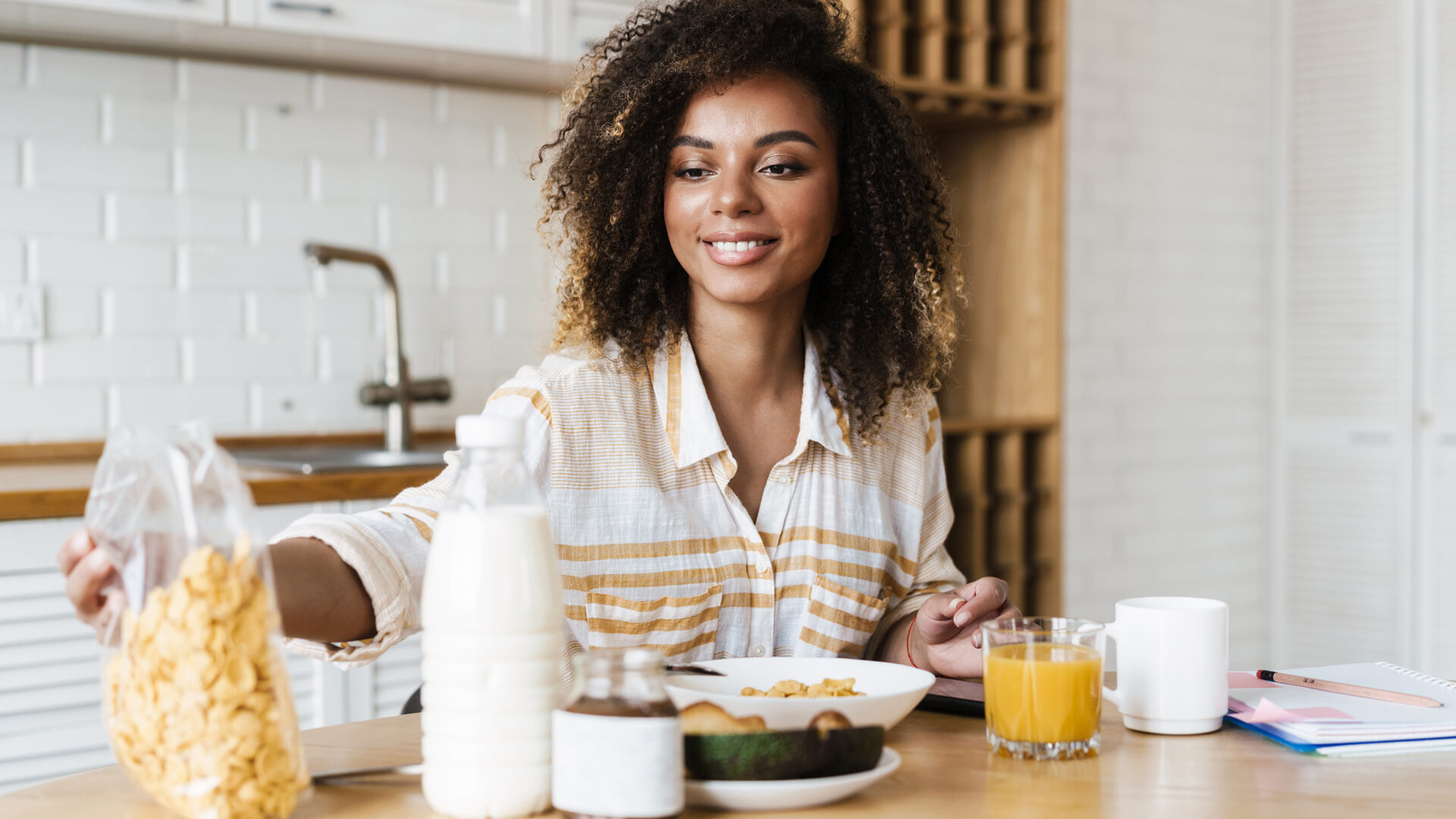 vrouw aan tafel met een bord cornflakes, brood, avocado en een fles melk voor haar