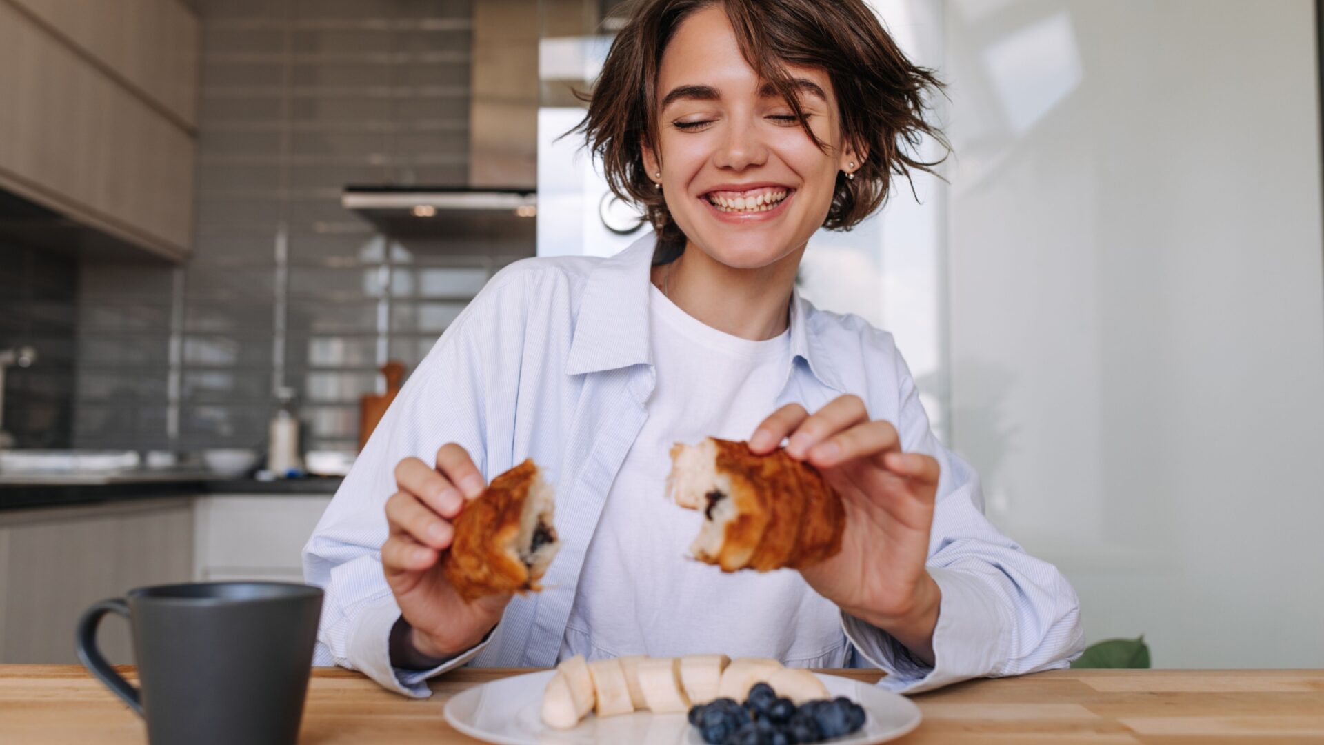 Vrouw aan tafel met een croissant in handen