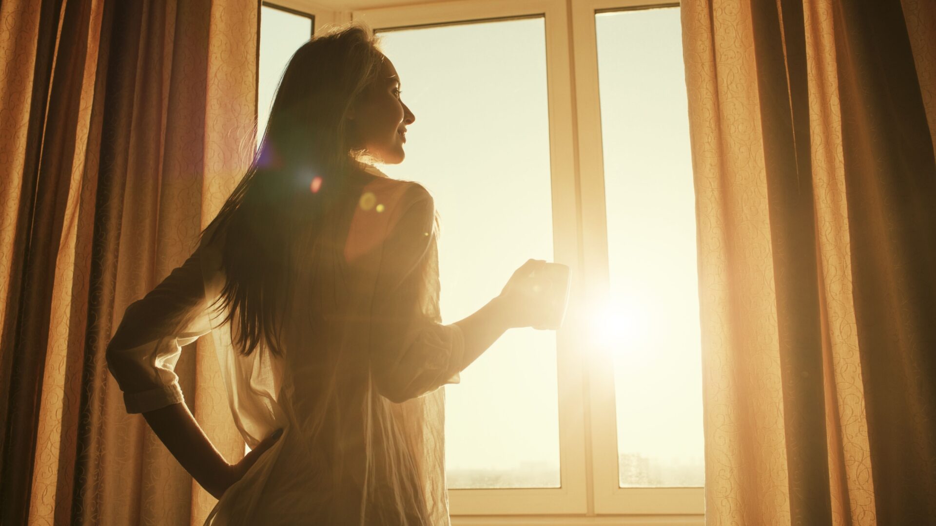 Vrouw voor het raam met een opkomende zon