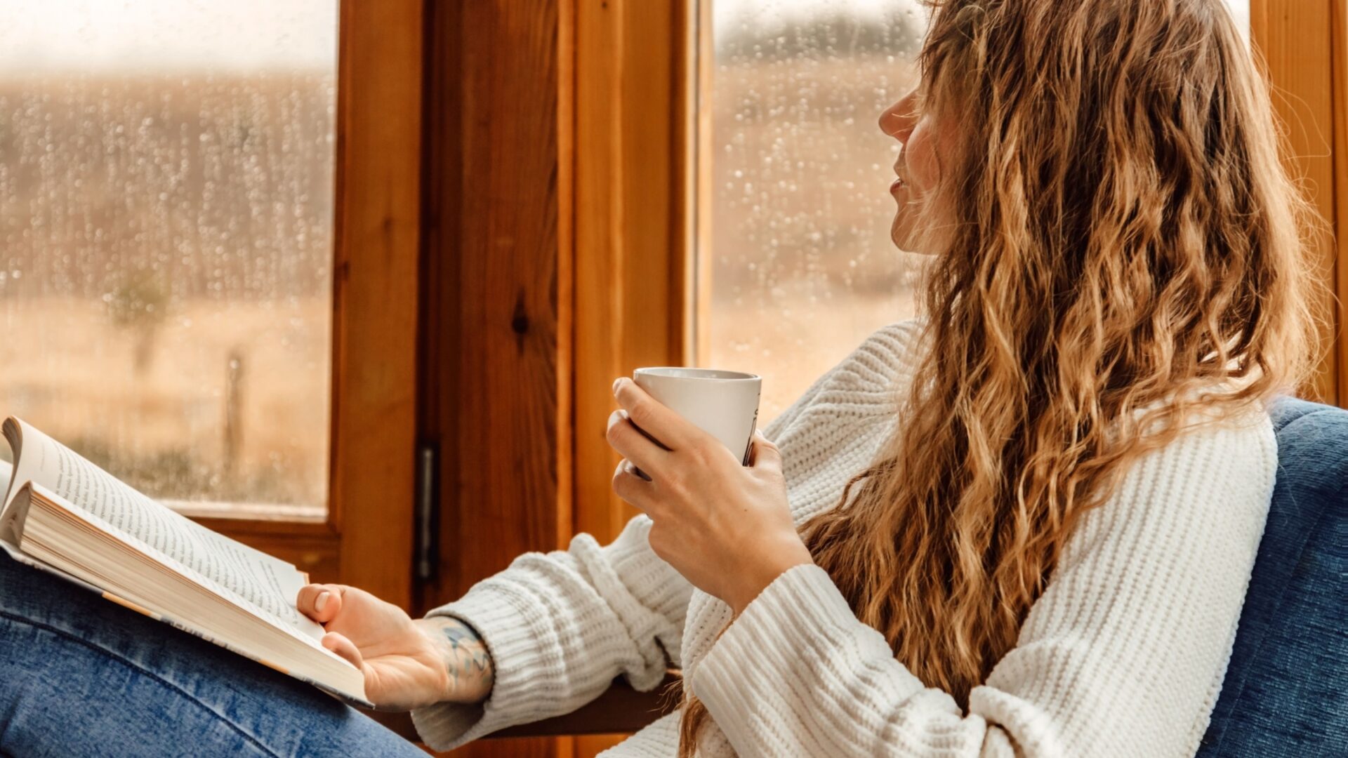 Vrouw met koffie en boek staart uit het raam