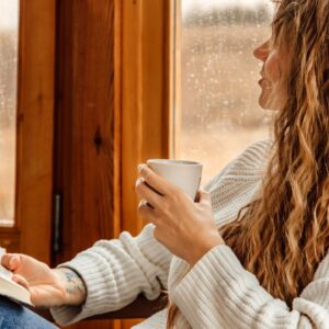 Vrouw met koffie en boek staart uit het raam