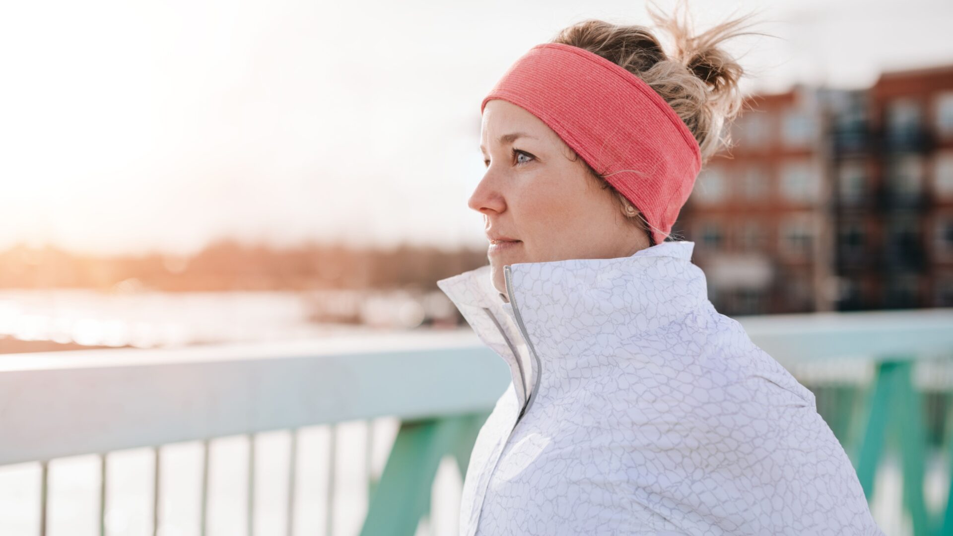 Vrouw met sport zip-up en haarband langs railing uitkijkend over water