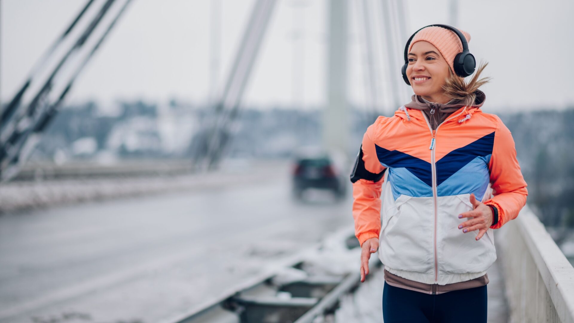 Hardlopende vrouw rent over een brug met muts en koptelefoon op