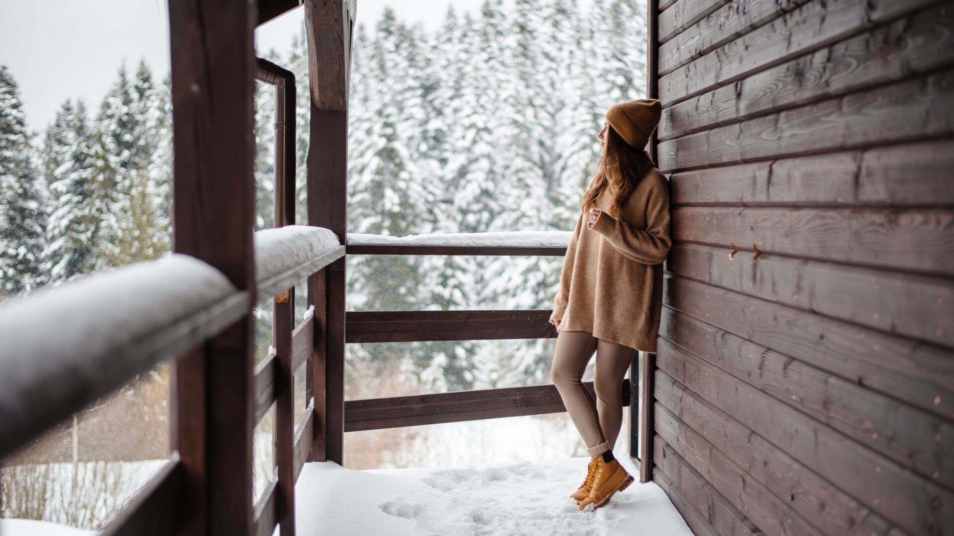 Vrouw in de sneeuw, leunend tegen een houten cabin