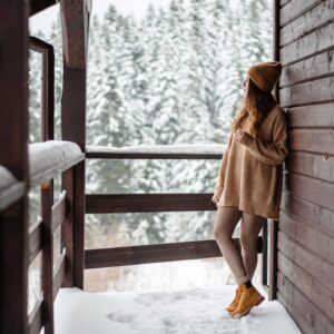 Vrouw in de sneeuw, leunend tegen een houten cabin